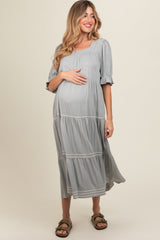 woman wearing a grey maternity dress with short puff sleeves and tiered skirt, gently holding her baby bump