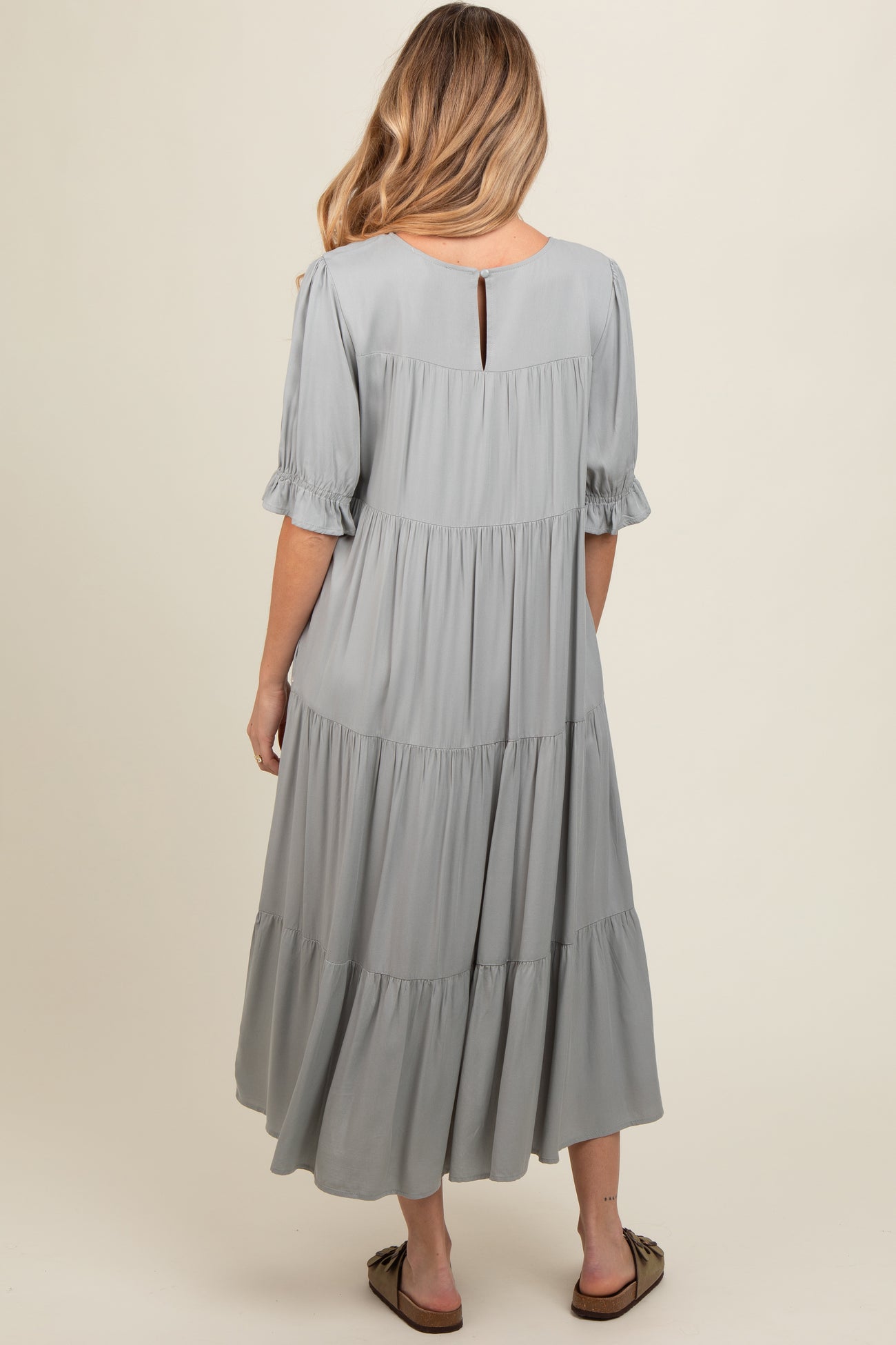 woman wearing a light grey tiered maternity dress, showing back view with short puff sleeves and keyhole detail