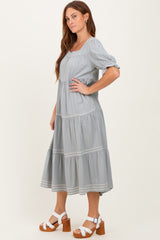 woman wearing a light gray midi dress with puff sleeves and tiered ruffles, paired with white heeled sandals