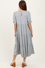 woman wearing a light gray tiered maxi dress with short puff sleeves and a keyhole back detail