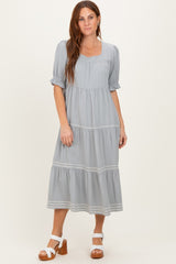 woman wearing a light gray tiered maxi dress with short puff sleeves and white embroidery details on the hem