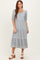 woman wearing a light gray tiered maxi dress with short puff sleeves and white embroidery details on the hem