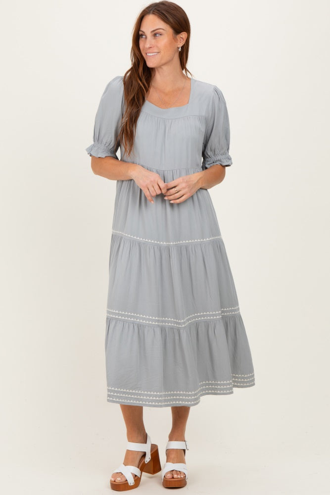 woman wearing a light gray tiered maxi dress with puff sleeves and embroidered details, standing and smiling