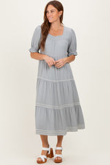 woman wearing a light gray tiered maxi dress with puff sleeves and embroidered details, standing and smiling