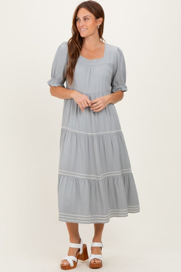 woman wearing a light gray tiered maxi dress with puff sleeves and embroidered details, standing and smiling