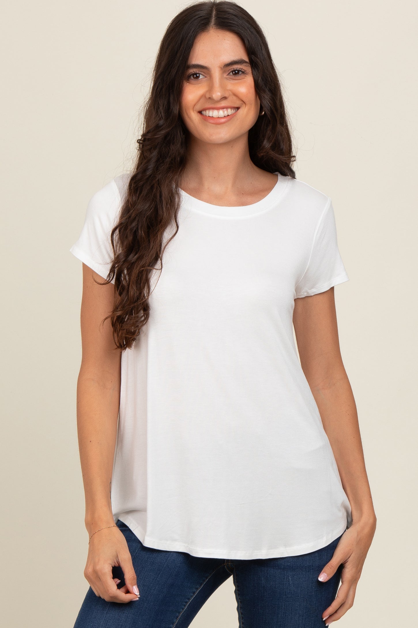 woman wearing a white short sleeve crew neck t-shirt and blue jeans, smiling with long wavy hair