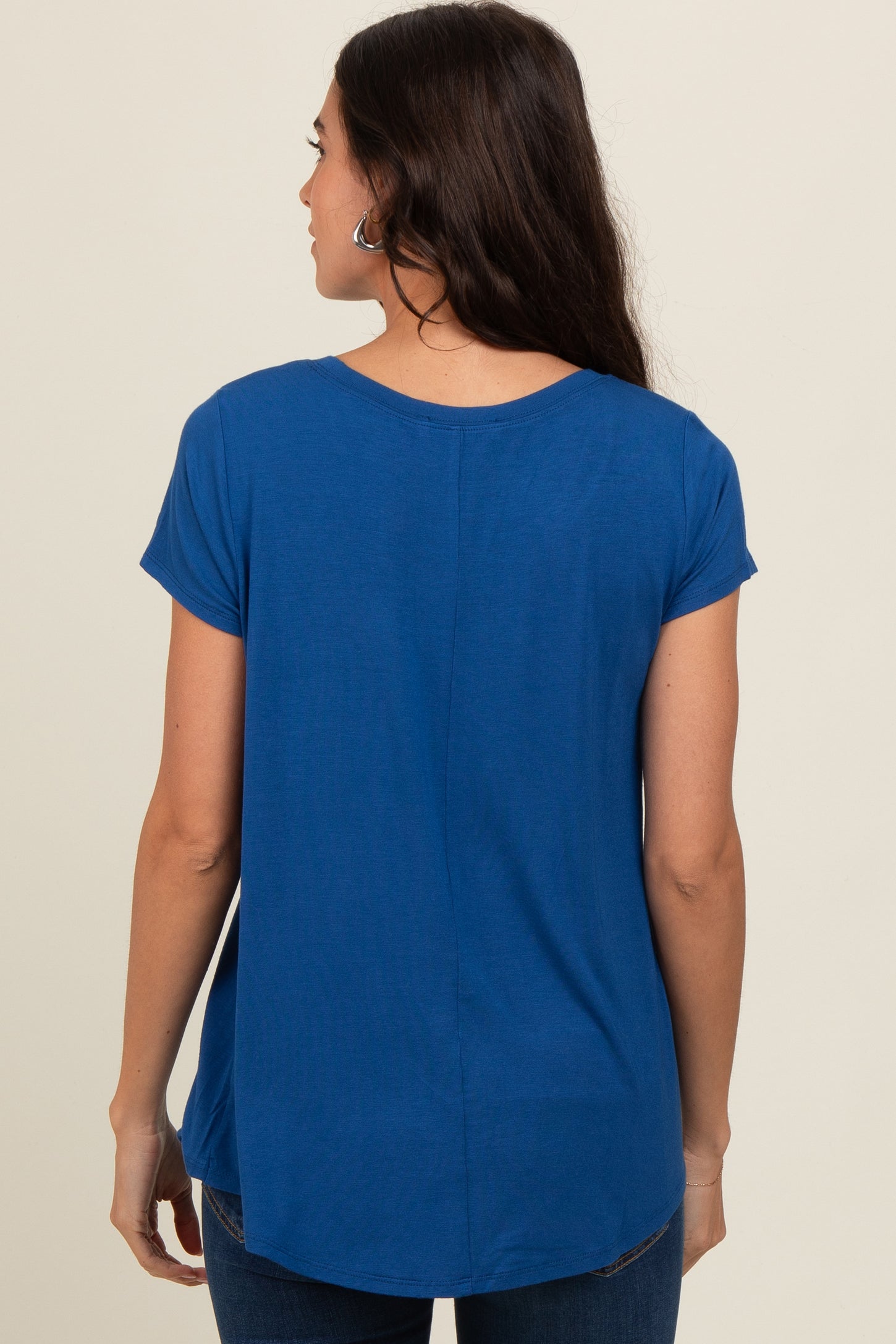 woman wearing a blue short sleeve casual top, showing a relaxed fit and rounded hem from the back
