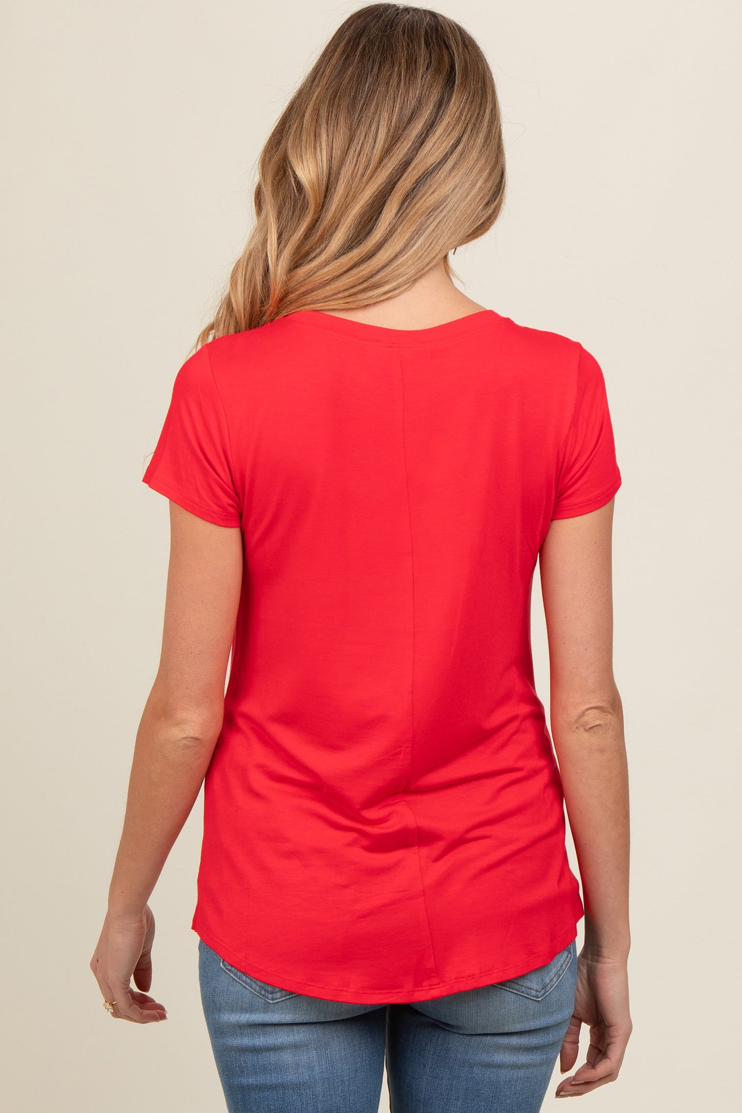 woman wearing a red short sleeve maternity top, seen from the back, paired with blue jeans