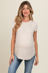 woman wearing a light beige short sleeve maternity top and showing her baby bump