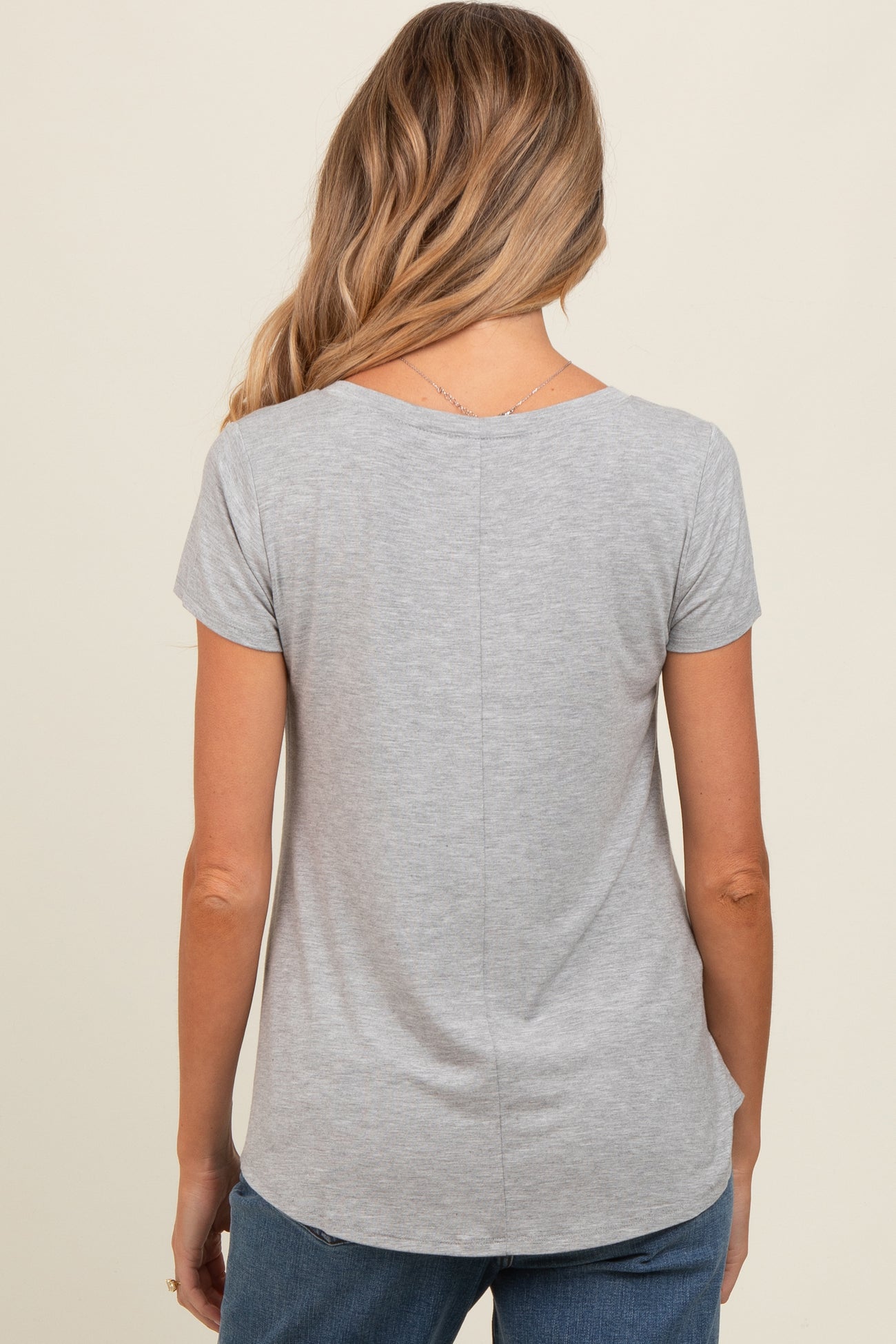 woman wearing a gray short sleeve maternity top, seen from the back, with a curved hem and casual style
