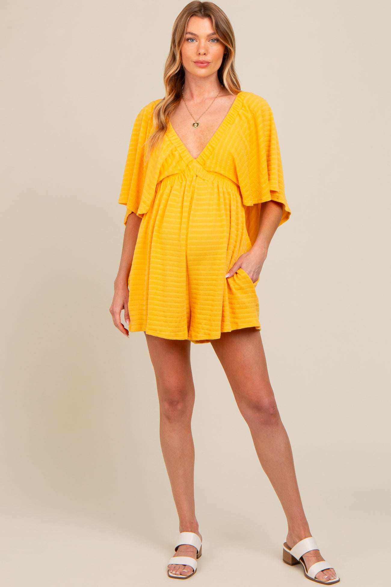 woman wearing a bright yellow striped maternity romper with short sleeves and side pockets