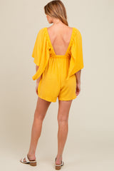woman wearing a yellow striped maternity romper with a deep v-back and flutter sleeves