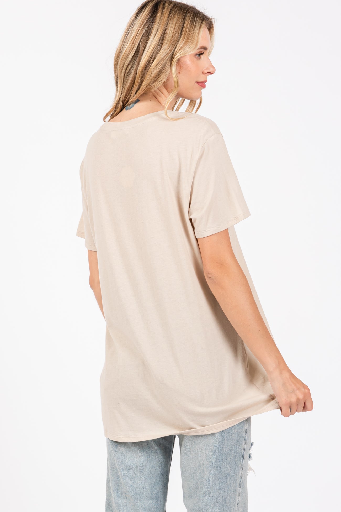 woman wearing a loose-fitting light beige short sleeve t-shirt and light blue distressed jeans, showing the back view