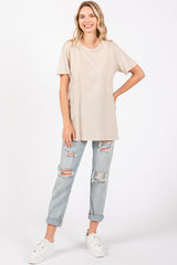 woman wearing a beige oversized t-shirt and distressed light blue jeans, smiling with hands on hips