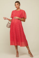 woman wearing a red floral maternity dress with short flutter sleeves and holding her baby bump