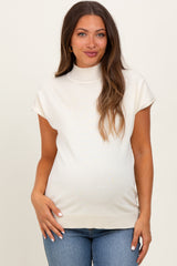 woman wearing a light beige maternity top with a mock neck and cap sleeves, showing her baby bump
