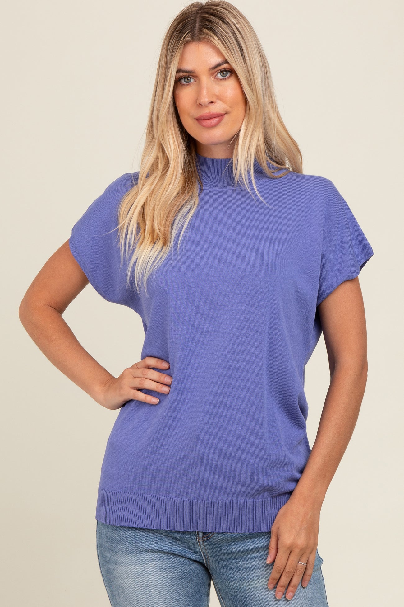 woman wearing a purple short sleeve sweater with a high neckline and relaxed fit, paired with jeans