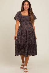 woman wearing a black floral print maternity dress with short puff sleeves and a tiered skirt, showcasing her baby bump