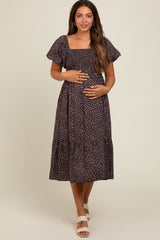 woman wearing a black floral maternity dress with short puff sleeves and a tiered skirt, holding her baby bump