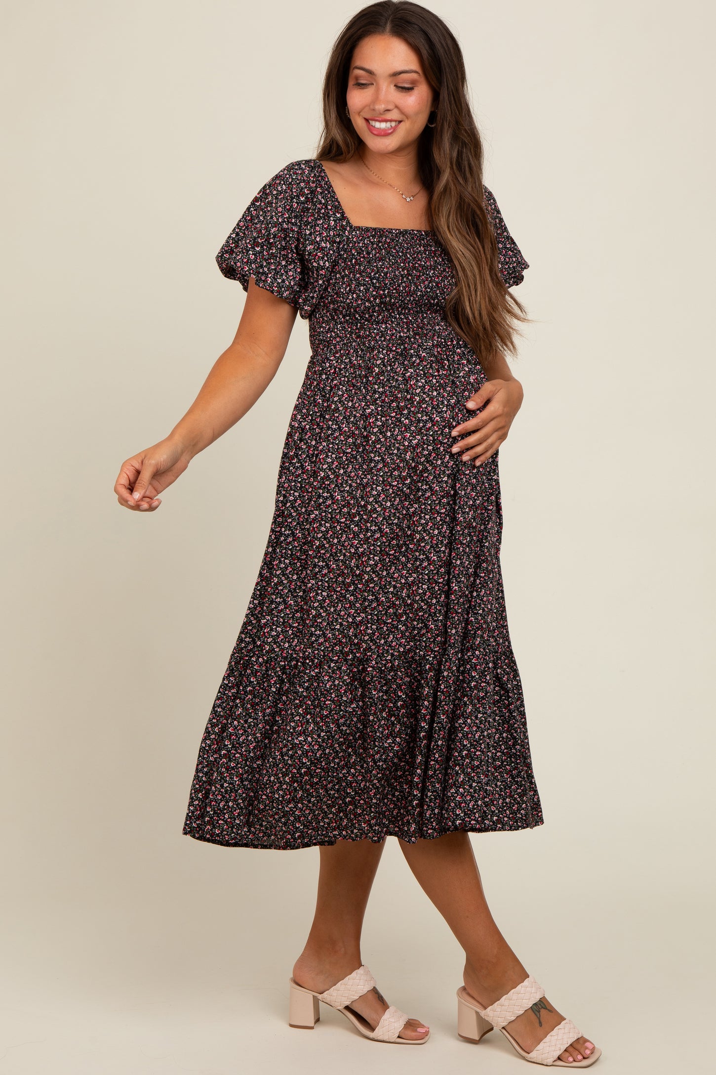 woman wearing a black floral maternity dress with puff sleeves and a flowing skirt, holding her baby bump