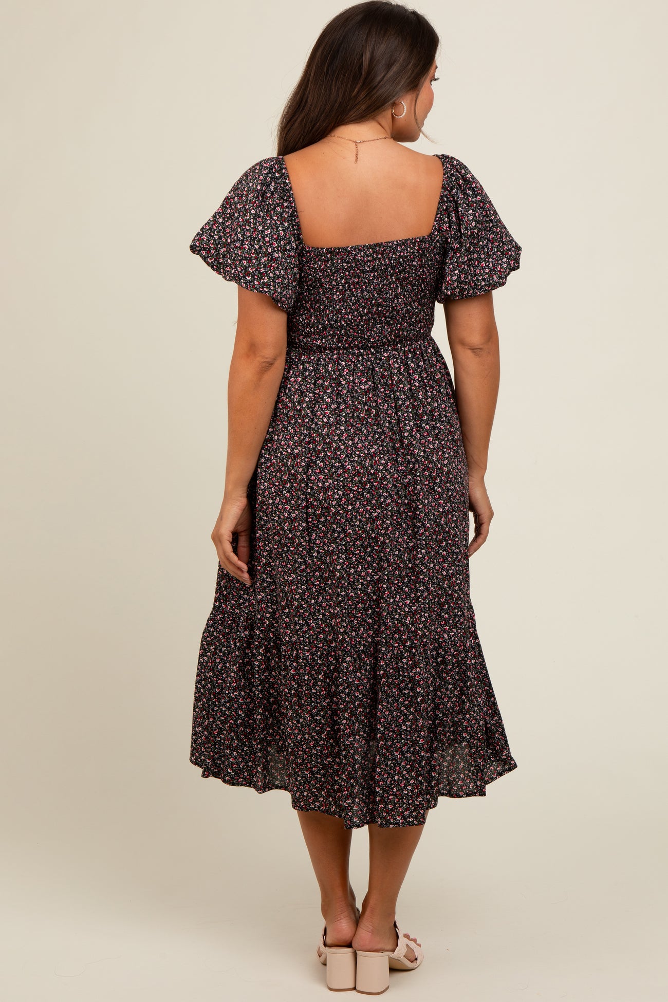 woman wearing a black floral midi maternity dress with puff sleeves and a smocked bodice from the back