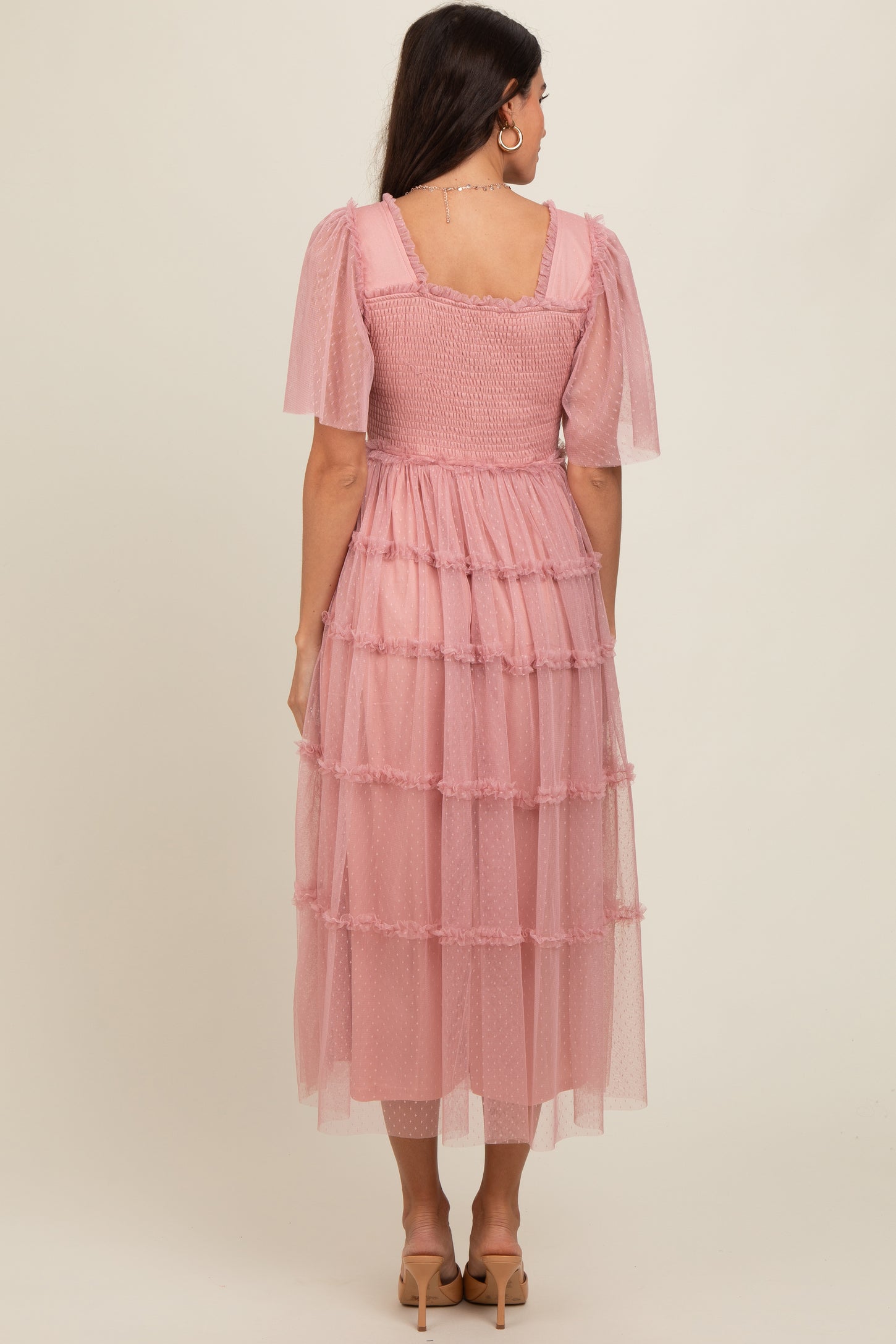 woman wearing a pink tiered tulle dress with short puff sleeves and a smocked bodice, viewed from the back