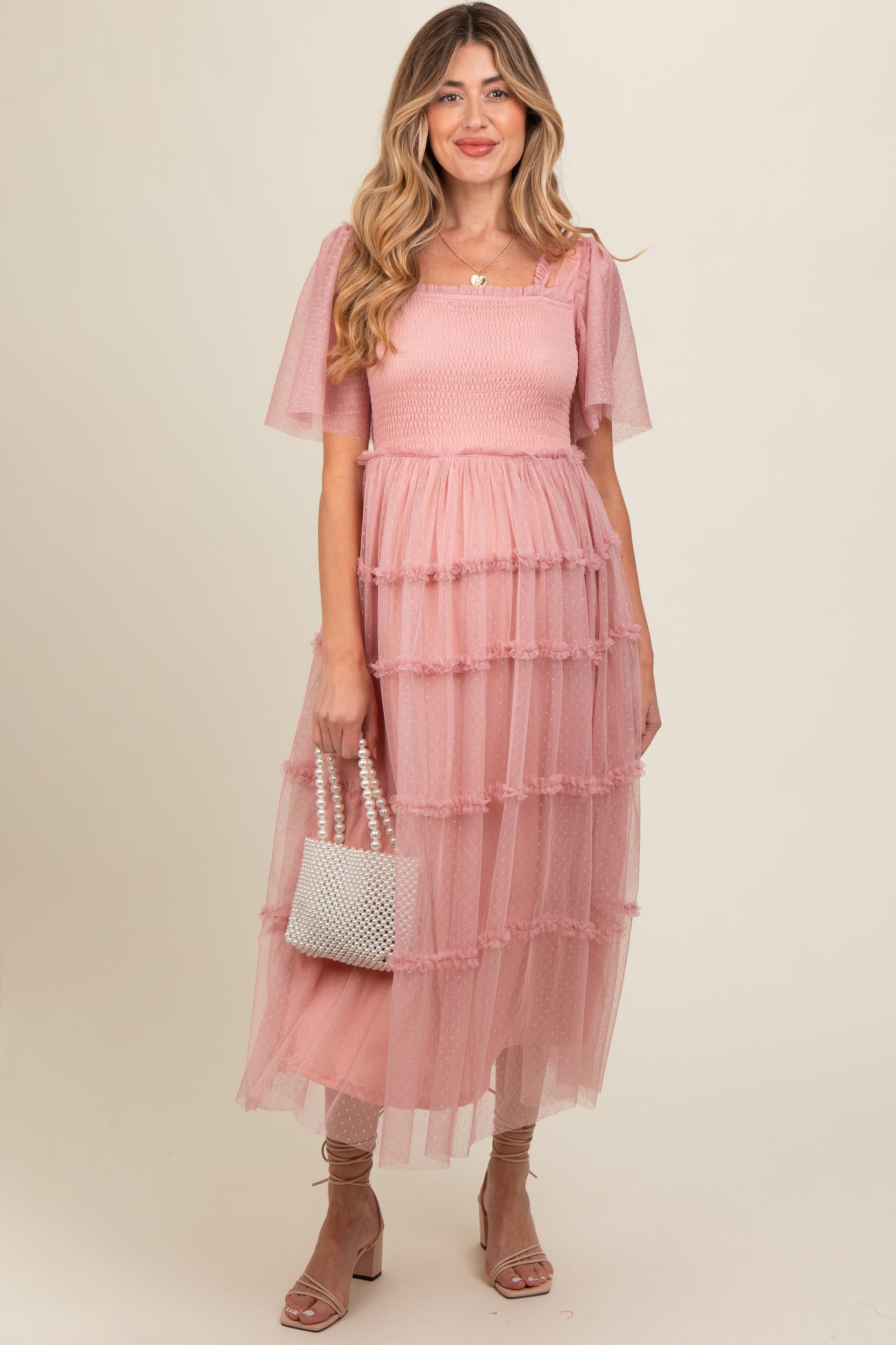 woman wearing a pink tiered tulle maternity dress with puff sleeves and holding a pearl-accented handbag