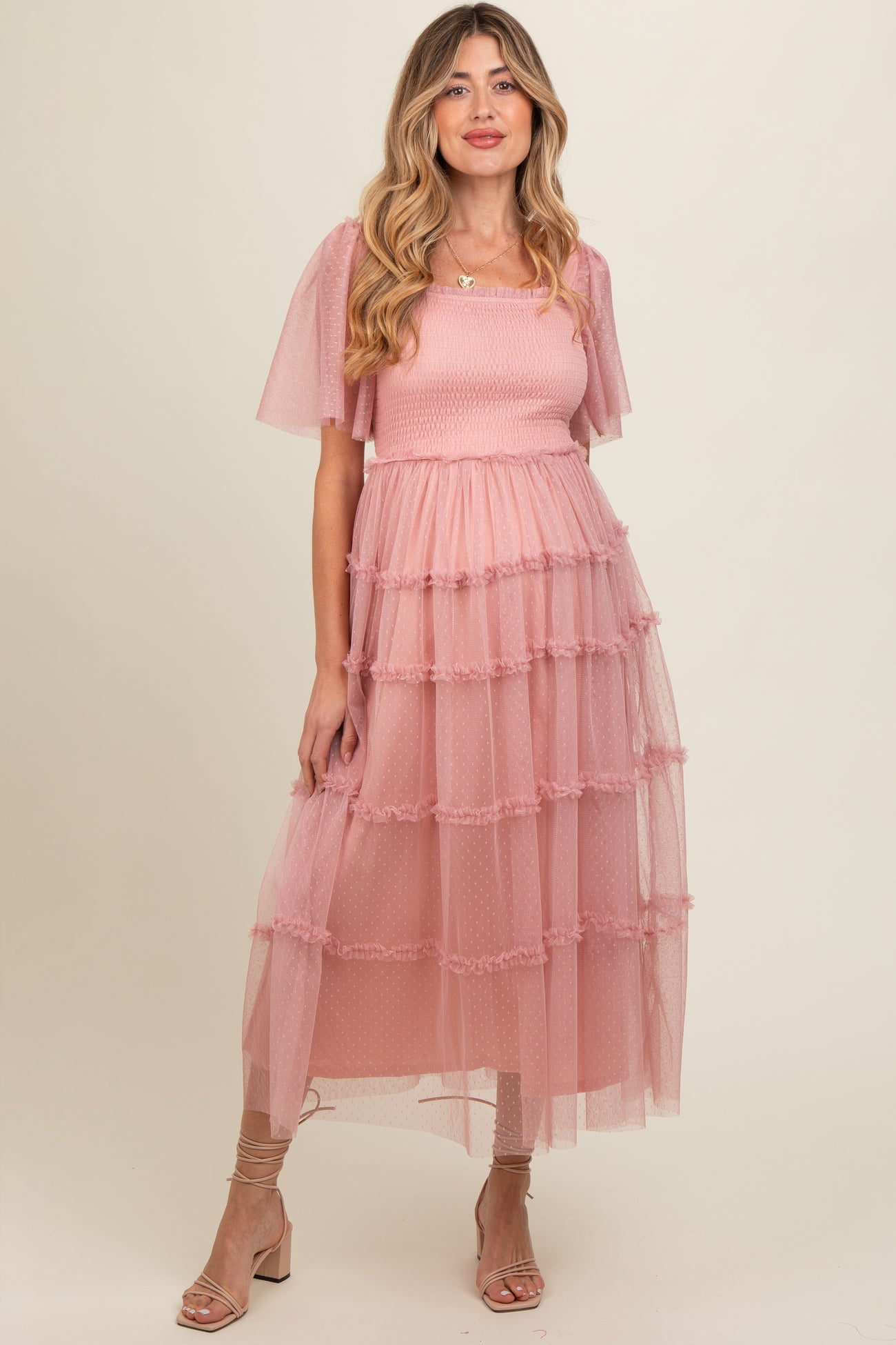 woman wearing a pink maternity dress with tiered tulle layers and flutter sleeves, featuring a fitted bodice and flowy skirt