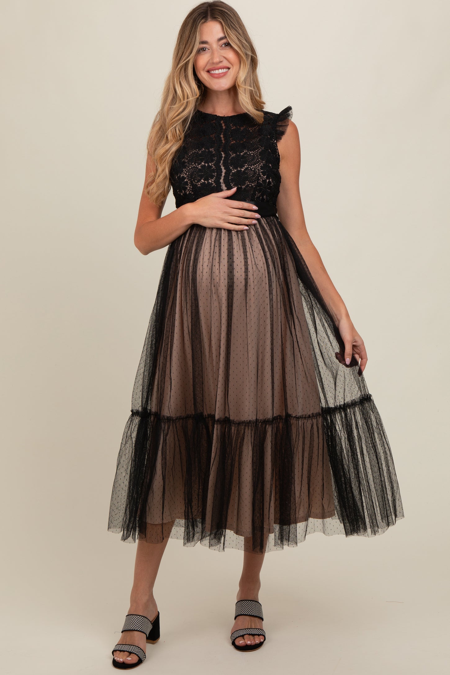 woman wearing a black lace and tulle maternity dress with a flowy skirt, holding her baby bump