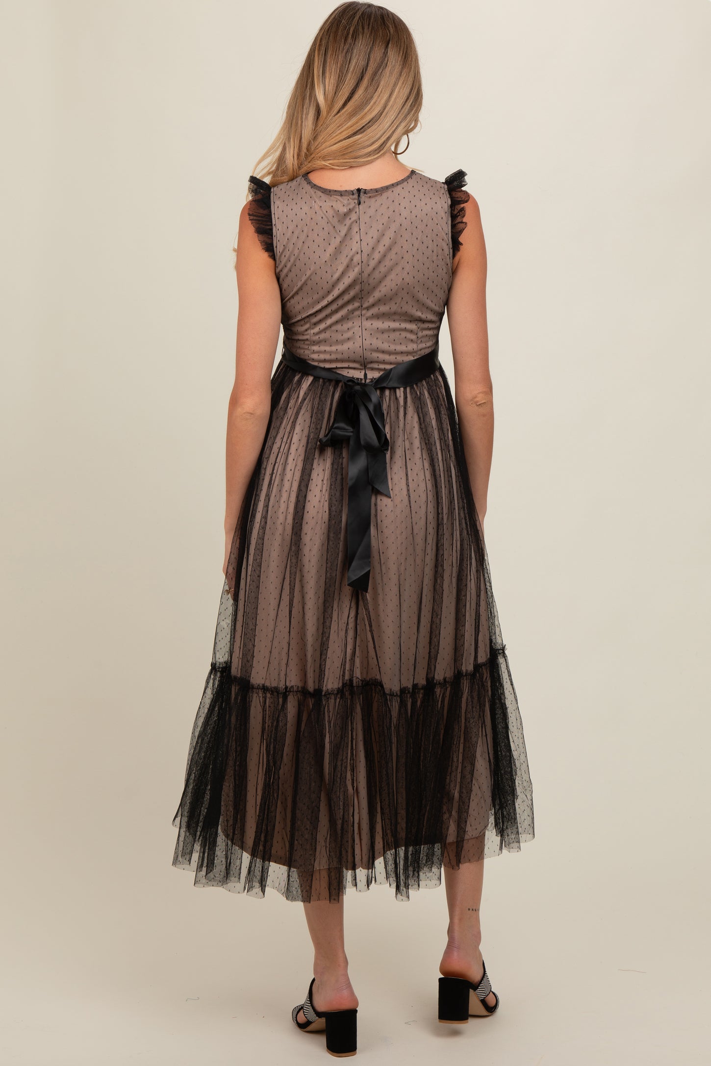 maternity wear in a brown polka dot dress with black tulle overlay and ruffled sleeves, model shown from the back