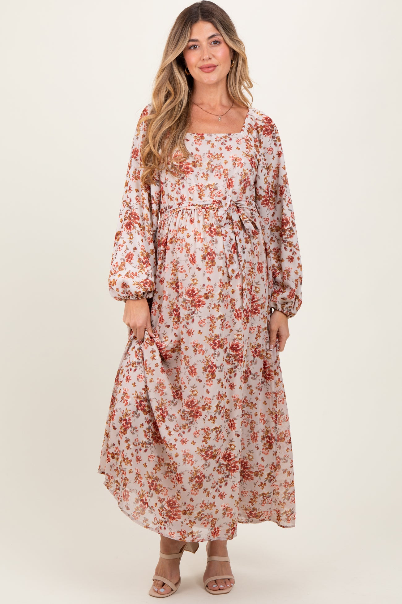 woman wearing a floral long sleeve maternity dress with a tie waist and flowing skirt, showcasing her baby bump