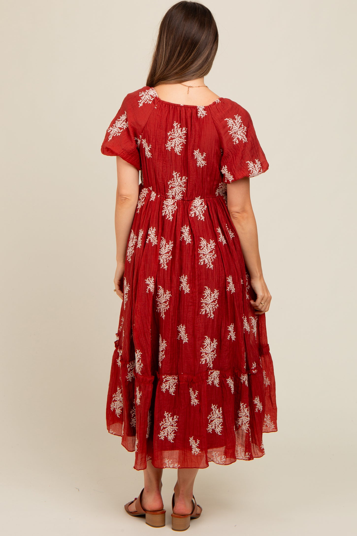 woman wearing a red maternity dress with floral embroidery and short sleeves, seen from the back