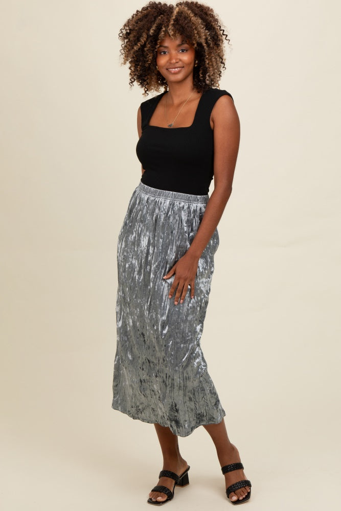 woman wearing a black fitted tank top and a silver pleated midi skirt, standing with a smile