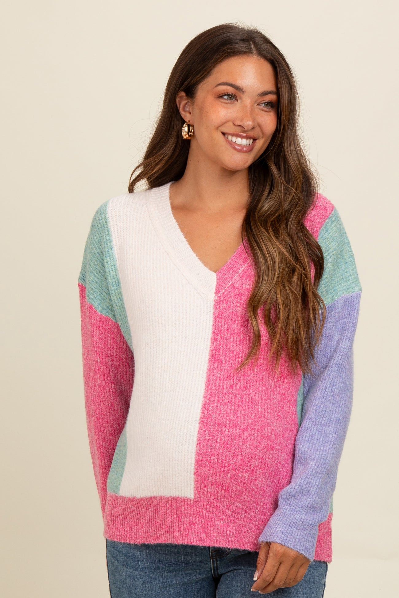 woman wearing a colorful v-neck maternity sweater with pink, light blue, and white block patterns and jeans