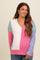 woman wearing a colorful v-neck maternity sweater with pink, light blue, and white block patterns and jeans