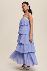 woman wearing a light purple tiered maxi dress with thin straps and lace detailing, standing against a neutral background