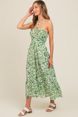 woman wearing a green and white floral maxi dress with a halter neck and ruched bodice, smiling and posing sideways