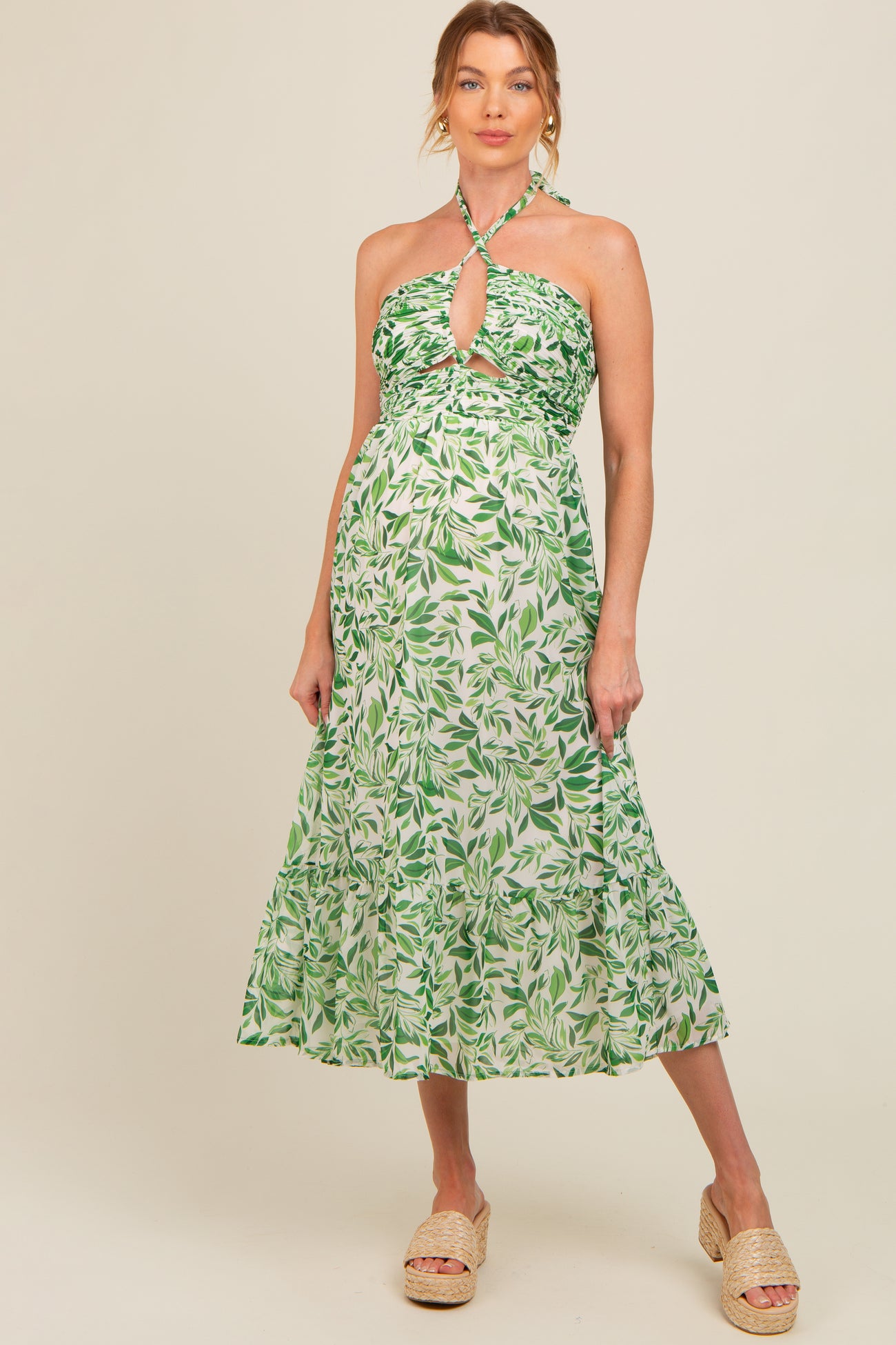 woman wearing a green and white leaf print maternity dress with a halter neckline and tiered skirt, showing her baby bump