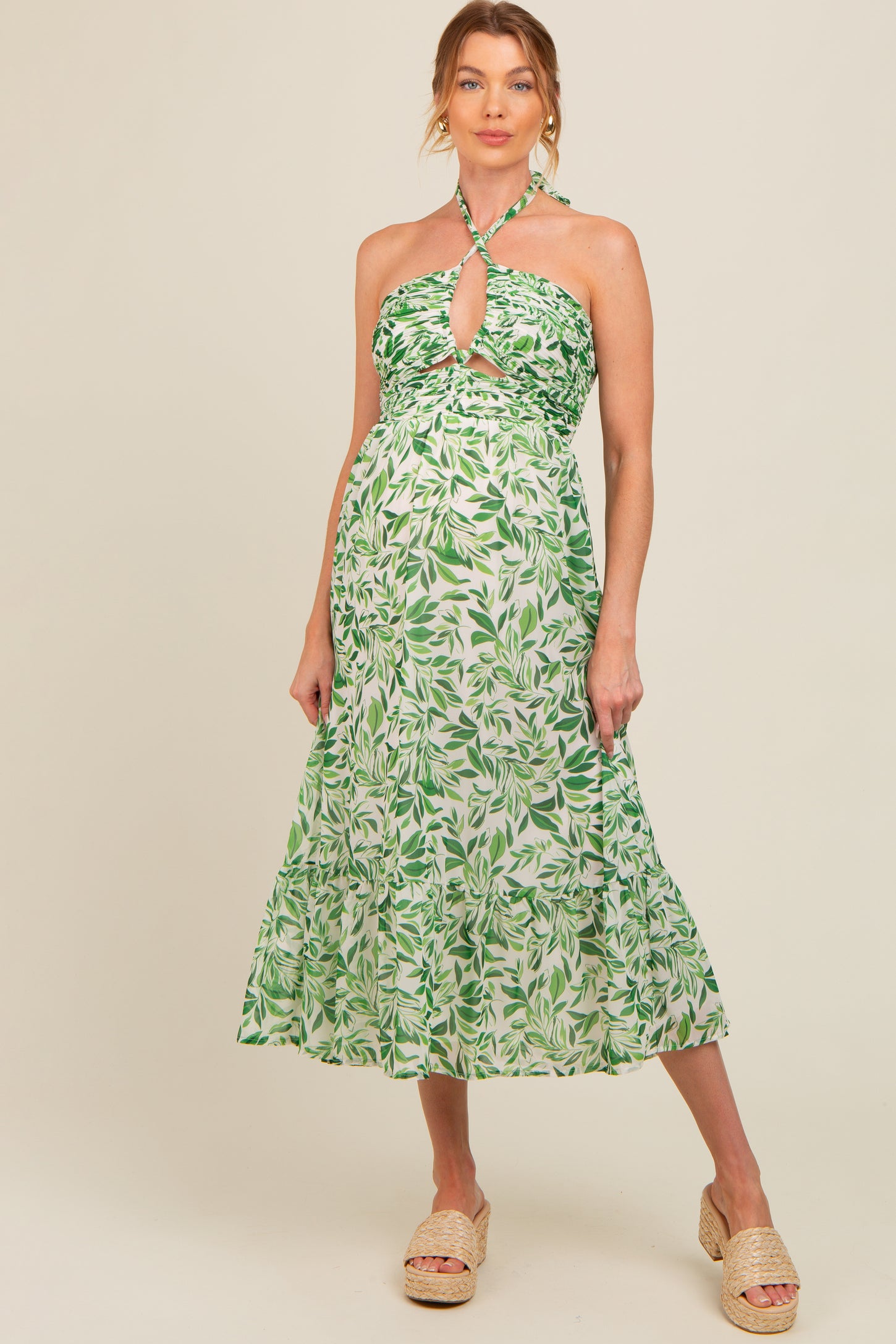 woman wearing a green and white leaf print maternity dress with a halter neckline and tiered skirt, showing her baby bump