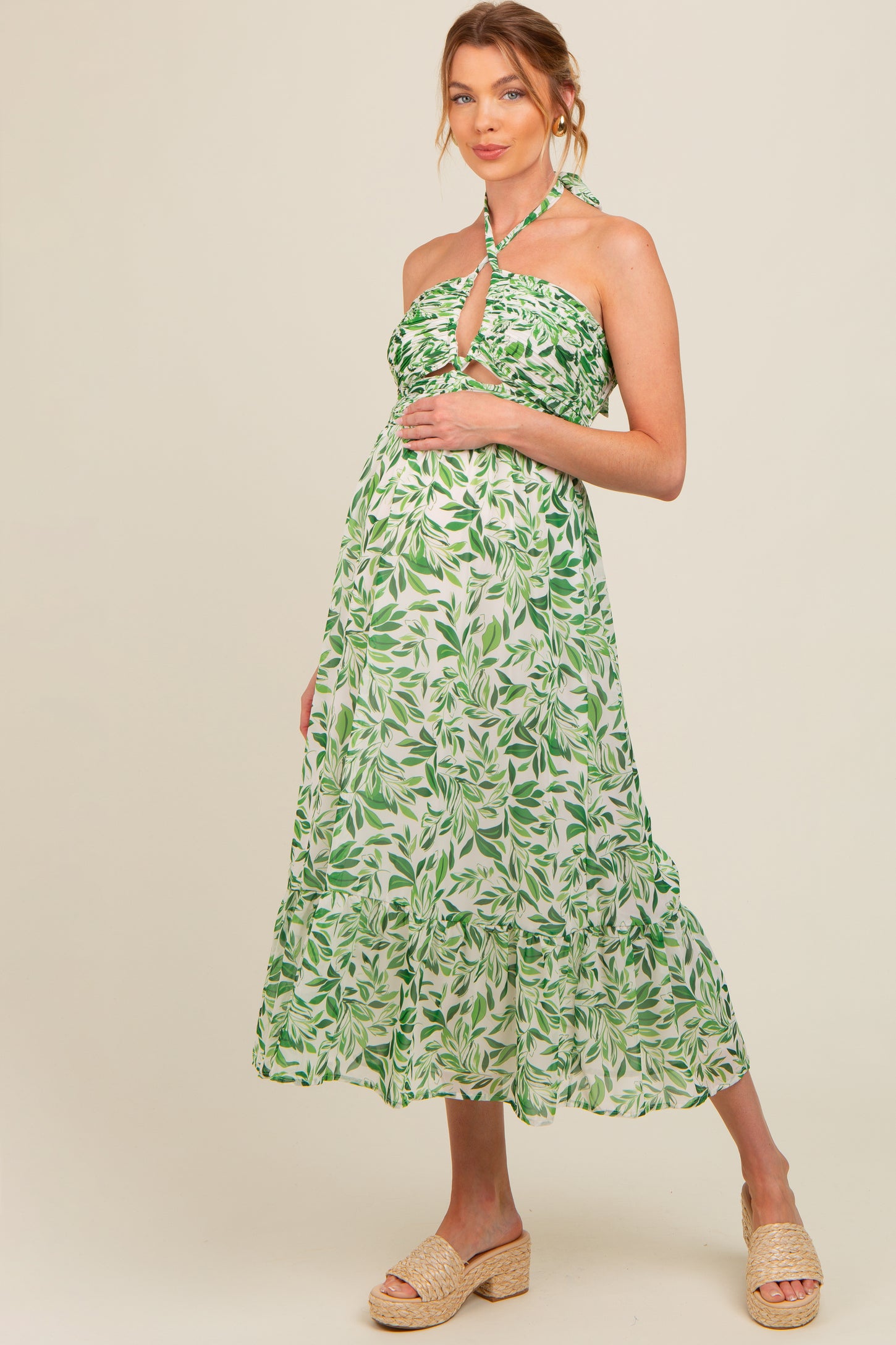 woman wearing a green leaf patterned maternity dress with a halter neckline and holding her baby bump