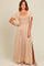 woman wearing a beige maxi dress with a smocked bodice and short flutter sleeves, showing a side slit