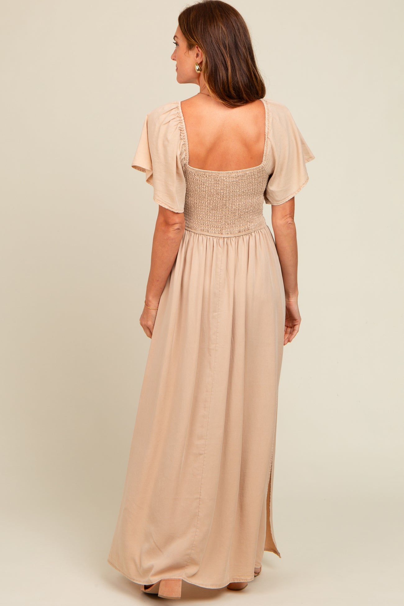 woman wearing a back view of a beige maxi dress with smocked bodice and flutter sleeves