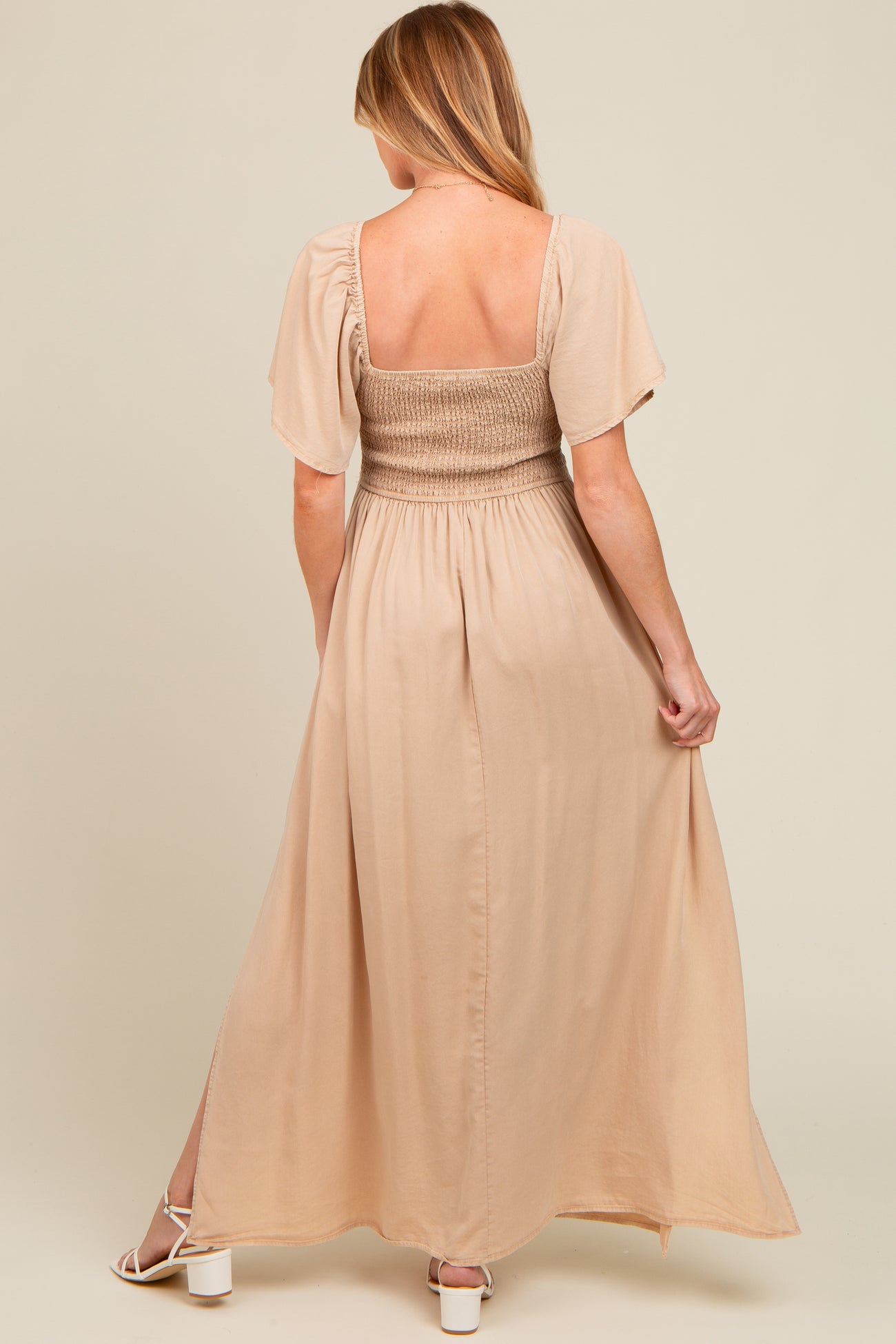 woman wearing a beige maternity maxi dress with short sleeves and a smocked bodice, showing her back