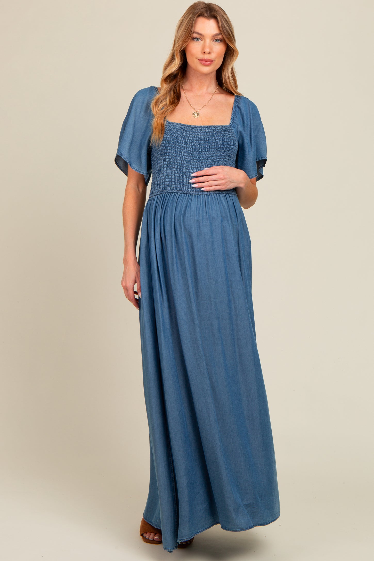 woman wearing a blue maternity maxi dress with a smocked bodice and short puff sleeves, holding her baby bump
