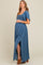 woman wearing a blue maternity maxi dress with a smocked bodice and side slit, holding her baby bump