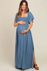 woman wearing a denim blue maternity maxi dress with short flutter sleeves and a smocked bodice, holding her baby bump