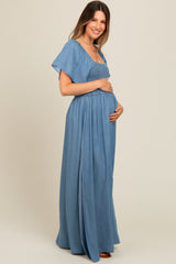 woman wearing a light blue maternity maxi dress with smocked bodice and flutter sleeves, gently cradling her baby bump