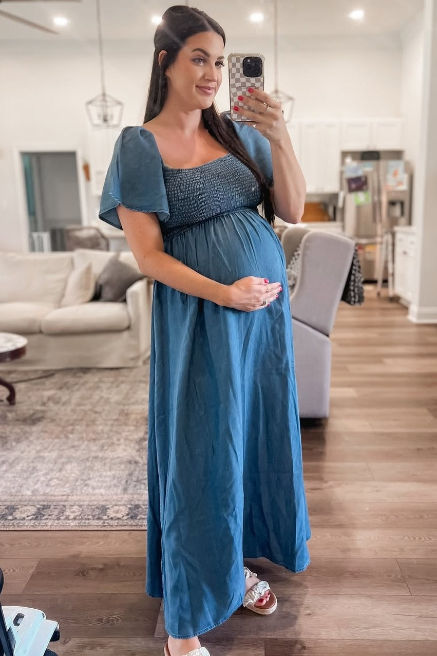 woman wearing a dark teal maternity dress with a smocked bodice and short puff sleeves, holding her baby bump