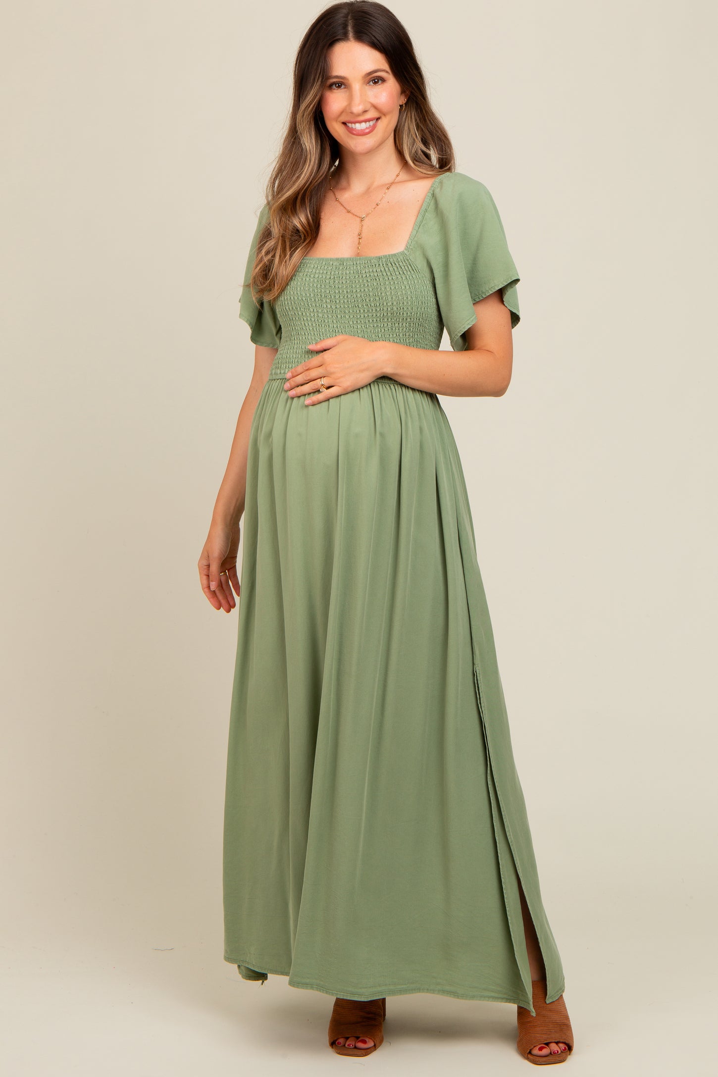 woman wearing a sage green maternity maxi dress with a smocked bodice and flutter sleeves, showing a baby bump