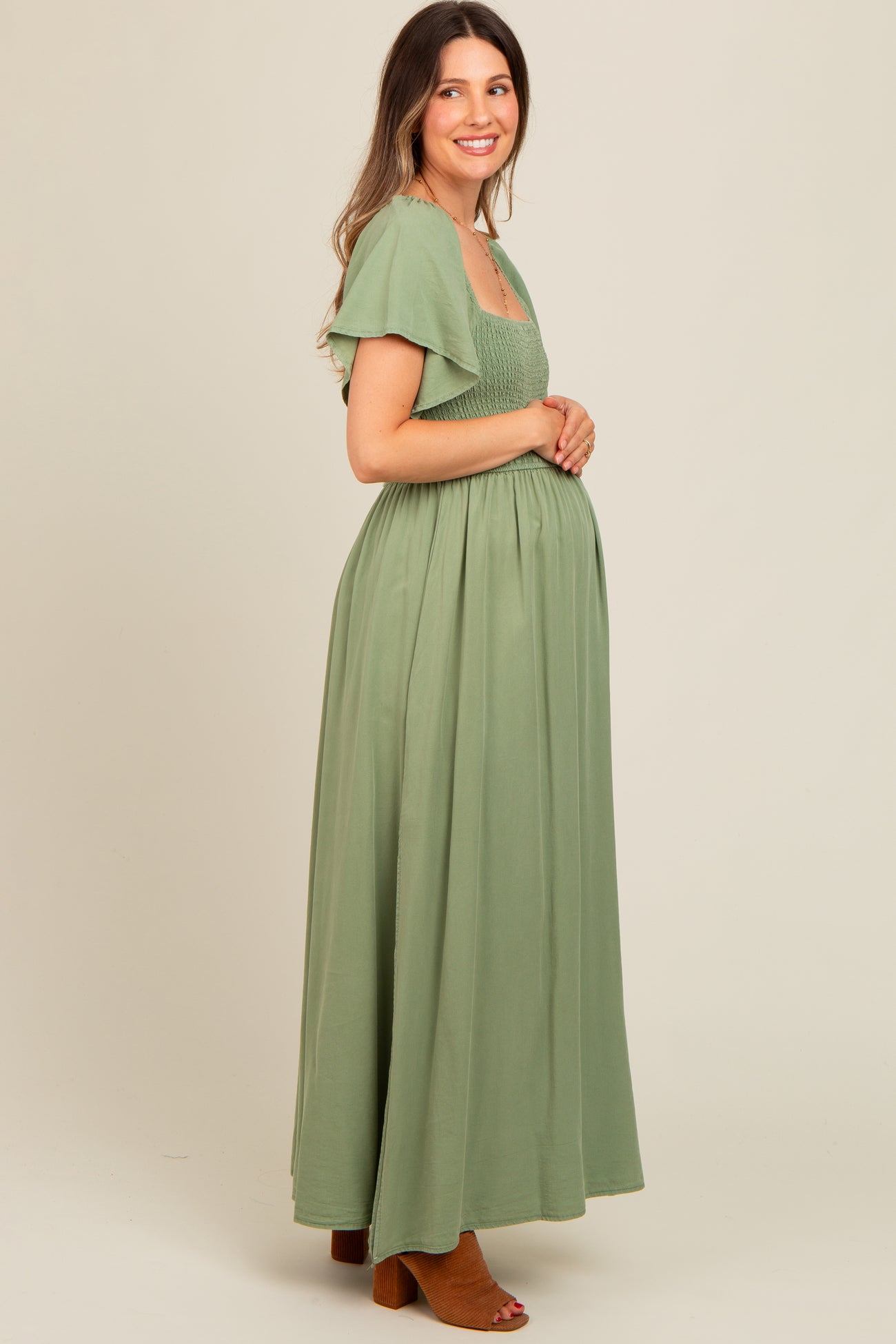 woman wearing a sage green maternity maxi dress with smocked bodice and flutter sleeves, showcasing a baby bump